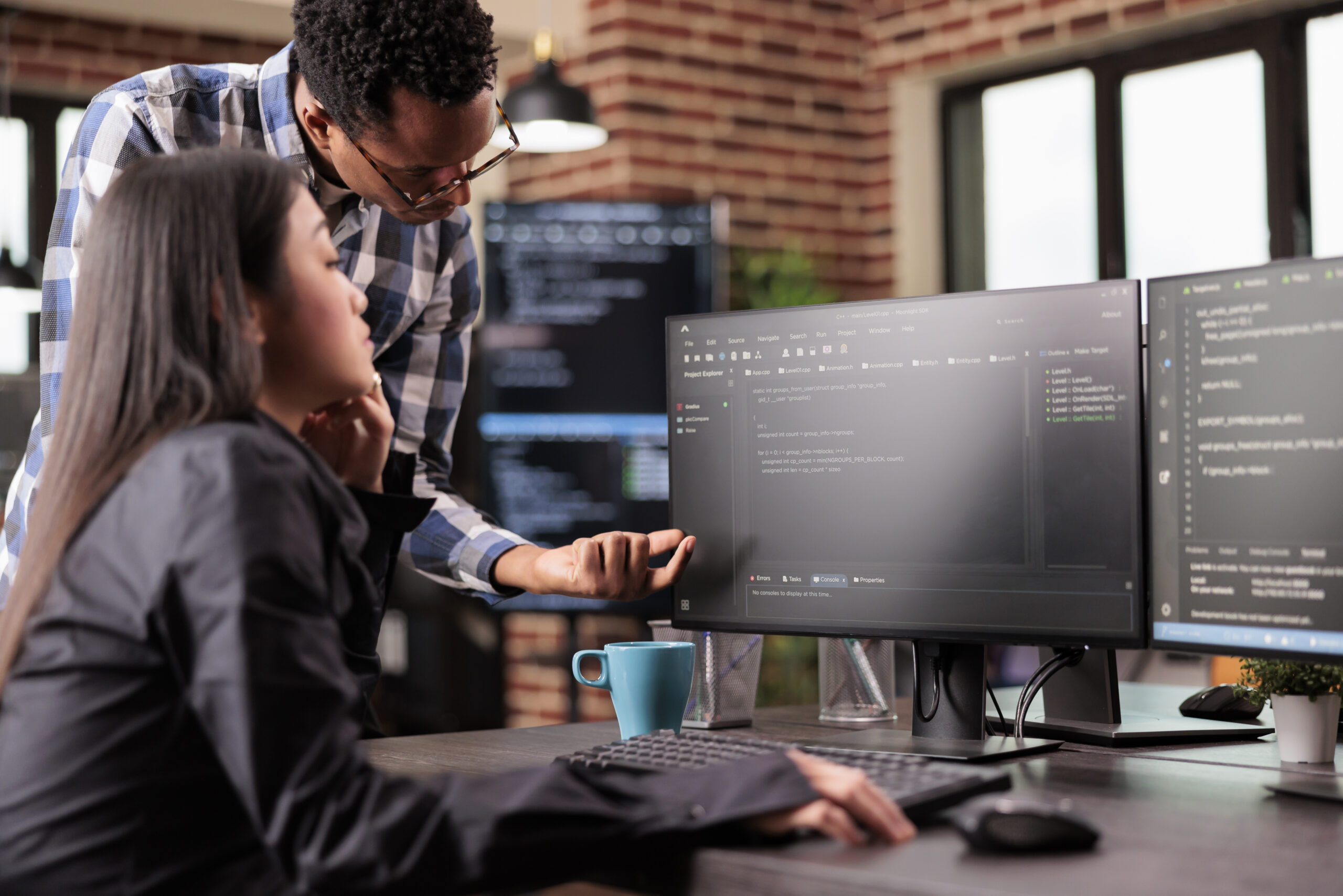 Diverse programmers discussing about html code compiling discovers errors, standing in front of multiple screens in startup office. Software developers working on server interface development.